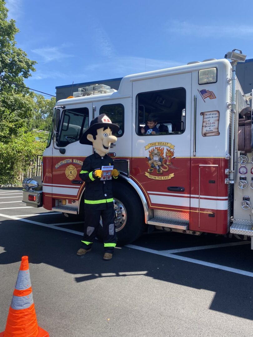 Firefighter mascot posing beside red fire truck